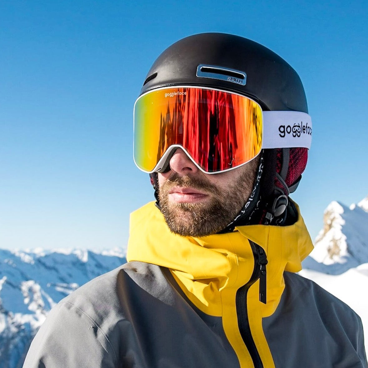 A man stands against a snowy mountain landscape, wearing a black ski helmet and Goggleface&
